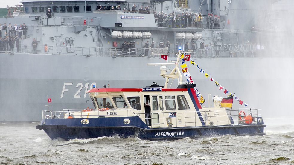 Boot des Hafenkapitäns vor der Fregatte der deutschen Marine, die Mecklenburg-Vorpommern: Wie viel ein Kapitän verdient, unterscheidet sich je nach Arbeitgeber. Foto: IMAGO / Zoonar