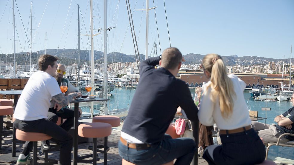 Touristen sitzen in der Sonne auf einer Terrasse in einem Restaurant am Hafen von Palma. Foto: dpa/Clara Margais