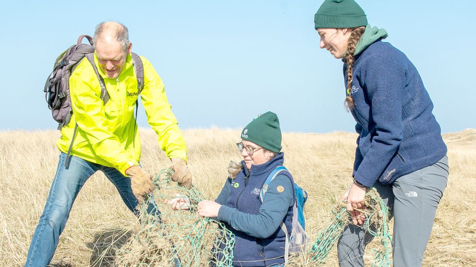 Mühsam klauben diese Bund-Aktivisten ein altes Fischernetz vom Strand auf Borkum auf. Plastikmüll stellt ein großes Problem für die Insel dar. Foto: Bund