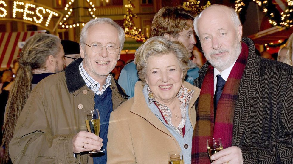 Die Schauspieler Joachim Hermann Luger (Hans Beimer, links) und die Schauspieler Marie-Luise Marjan (Mutter Beimer) und Bill Mockridge (Erich Schiller, rechts) posieren in der Außenkulisse mit Sektgläsern nach der Live-Ausstrahlung der 1559. Folge im Dezember 2015. Foto: picture alliance / dpa