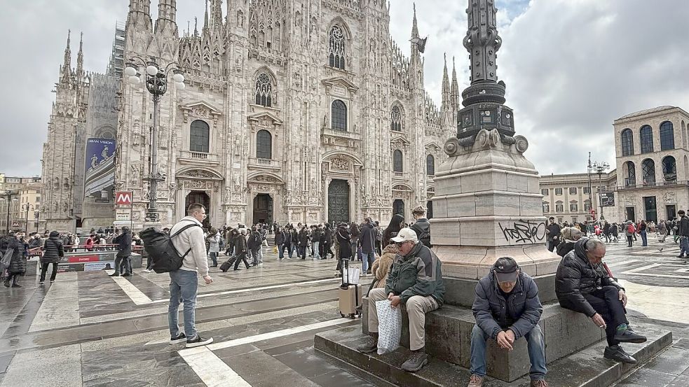 Trotz Rauchverbots sitzen zwei Männer mit Zigaretten in der Hand vor dem Mailänder Dom. Foto: Christoph Sator/dpa