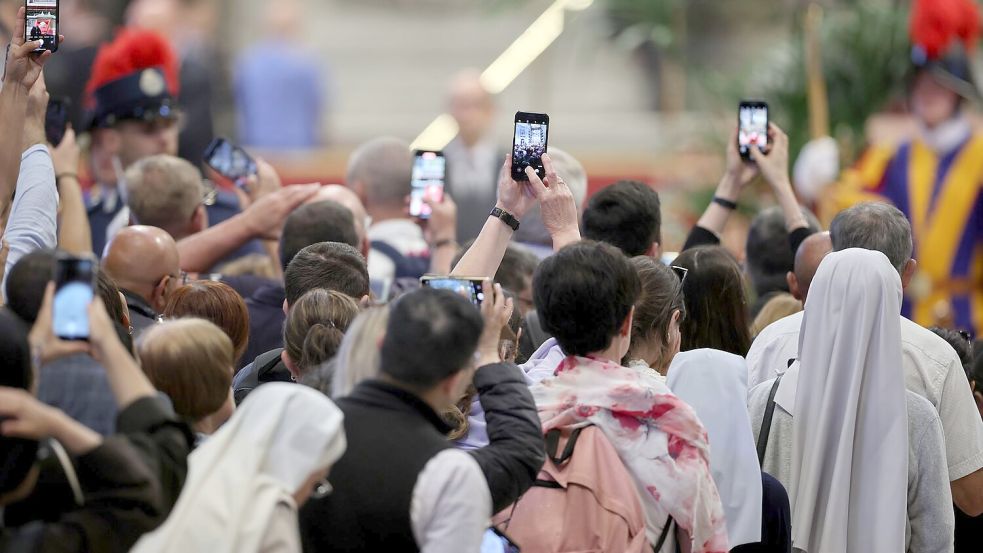 Mit den Smartphones machen Gläubige ein Foto vom toten Papst. Foto: Christoph Reichwein/dpa