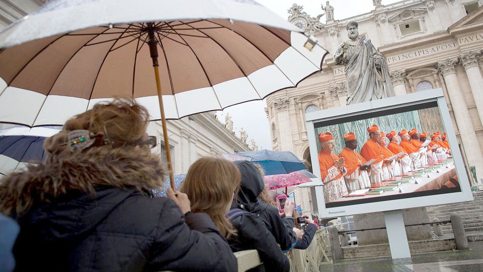 Gläubige beobachten bei der vergangenen Papstwahl im Jahr 2013 auf dem Petersplatz im Vatikan auf Videomonitoren den Einzug der Kardinäle in der Sixtinischen Kapelle. Foto: dpa/Michael Kappeler