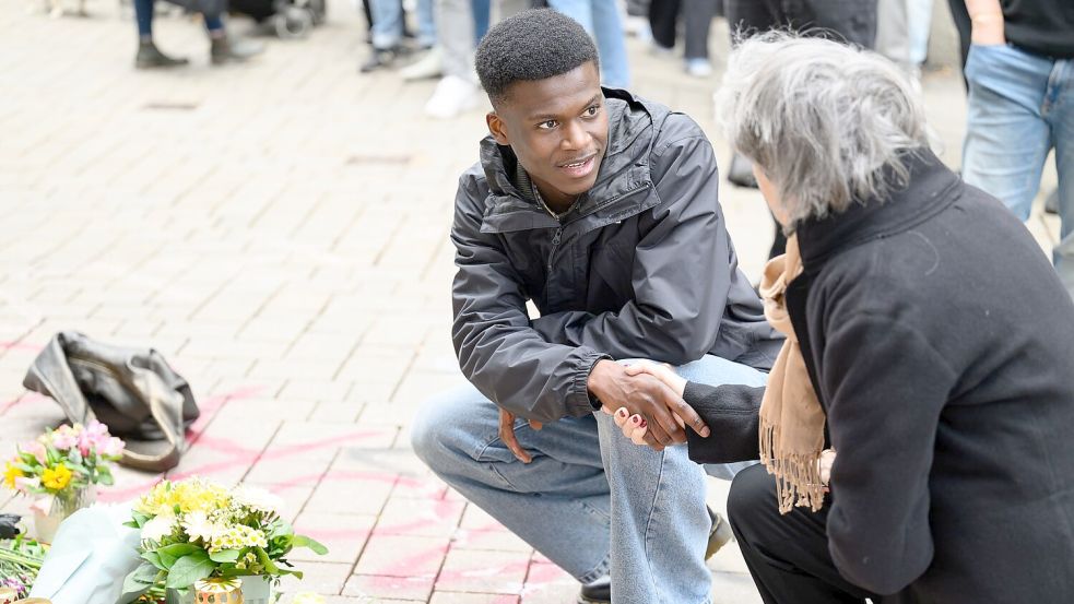 Suraj Mailitafi (l) von der Initiative „Gerechtigkeit für Lorenz“ spricht mit einer Passantin an dem Ort, an dem der 21-Jährige von der Polizei erschossen wurde. Foto: Izabela Mittwollen/dpa
