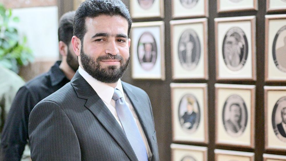 Anas Chattab ist erst seit Ende März Innenminister von Syrien. Hier steht er vor Fotos seiner Vorgänger im Amt. Die Bilder einiger Ex-Minister haben die neuen Machthaber entfernt. Foto: Sebastian Gollnow/dpa