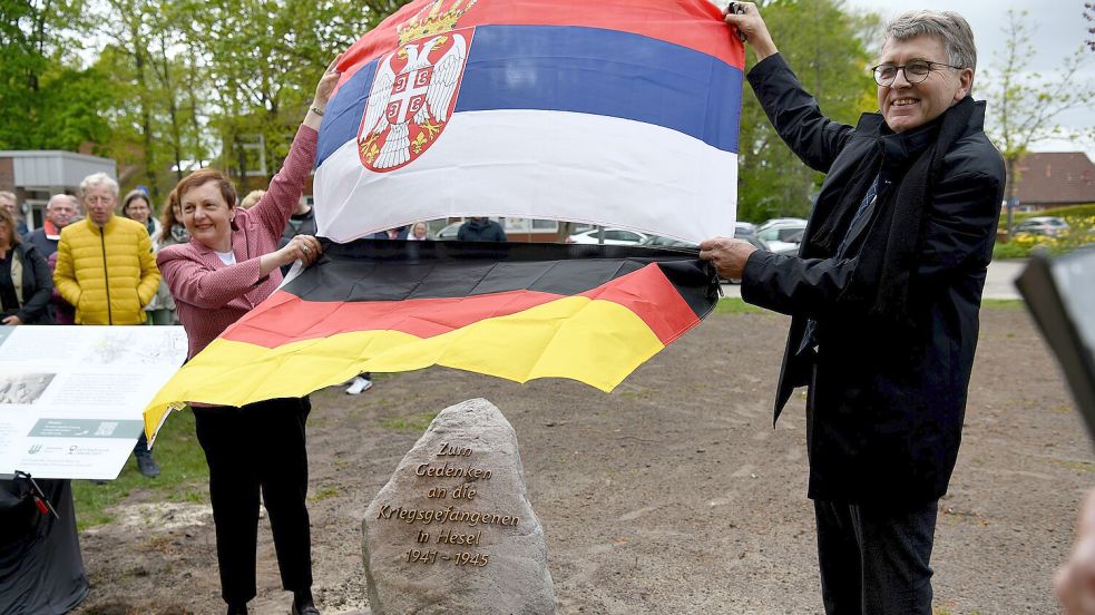 Milena Nikolić und Gerd Dählmann ziehen die serbische und die deutsche Flagge von dem Gedenkstein in Hesel. Links daneben steht die Infotafel. Foto: Stromann