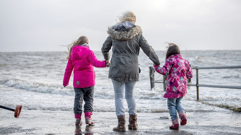 Es ist ein fantastisches Schauspiel, wenn die Nordsee die Küste bedrängt und die Fluten ungeschützte Flächen überspülen: Eine Mutter steht Hand in Hand mit ihren Töchtern bei Sturmflut an der Wasserkante. Foto: Sina Schuldt/dpa