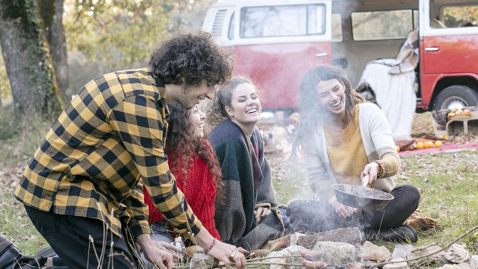 Mit einer Pfanne über dem Lagerfeuer wird das Kochen im Freien zum Genuss – die richtige Ausrüstung macht’s möglich. Foto: IMAGO / Westend61