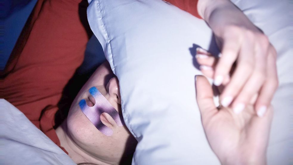 Eine Frau liegt mit einem Mundpflaster im Bett. Ob es hilft? (Illustration) Foto: Christoph Soeder/dpa