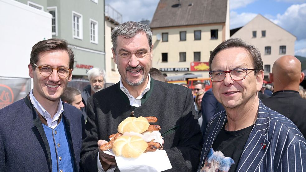Markus Söder (M.) hält Bratwurst-Semmeln in die Kamera. Foto: Felix Hörhager/dpa