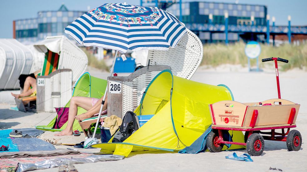 Sommer, Sonne, Norddeich: Ein Bollerwagen, ein Strandzelt und ein Sonnenschirm stehen neben einem Strandkorb am Strand. Foto: dpa/Hauke-Christian Dittrich/Archiv