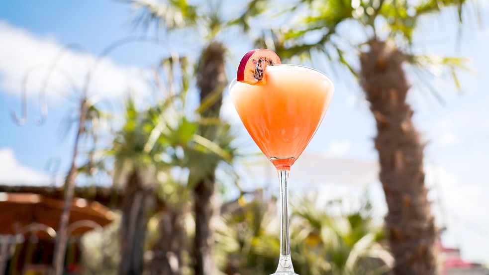 Ein Passionsfrucht Martini (auch Pornstar Martini oder Maverick Martini genannt) steht unter Palmen auf einem Tisch in einer Strandbar. Foto: Christian Charisius/dpa