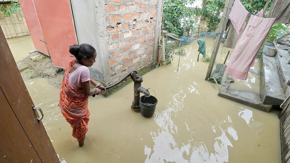 Eine Frau versucht in der überfluteten Umgebung ihres Hauses, Wasser zu sammeln. Foto: Uncredited/AP/dpa