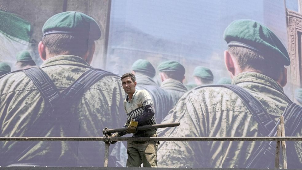 Ein Arbeiter steht auf dem Platz der Islamischen Revolution in Teheran, Iran, vor einem anti-israelischen Banner, das iranische Soldaten zeigt, die angeblich auf dem Weg sind, israelisches Gebiet anzugreifen. Foto: AP/Vahid Salemi