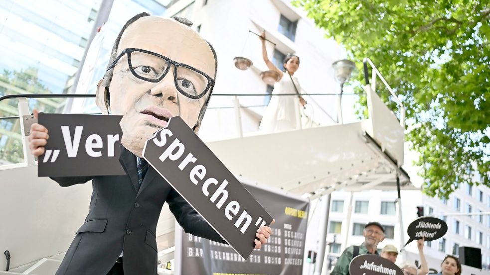 Ein Aktivist mit Merz-Maske zerbricht während einer symbolischen Protestaktion von Kabul Luftbrücke und Campact ein Schild mit der Aufschrift „Versprechen“. Foto: Sebastian Christoph Gollnow/dpa