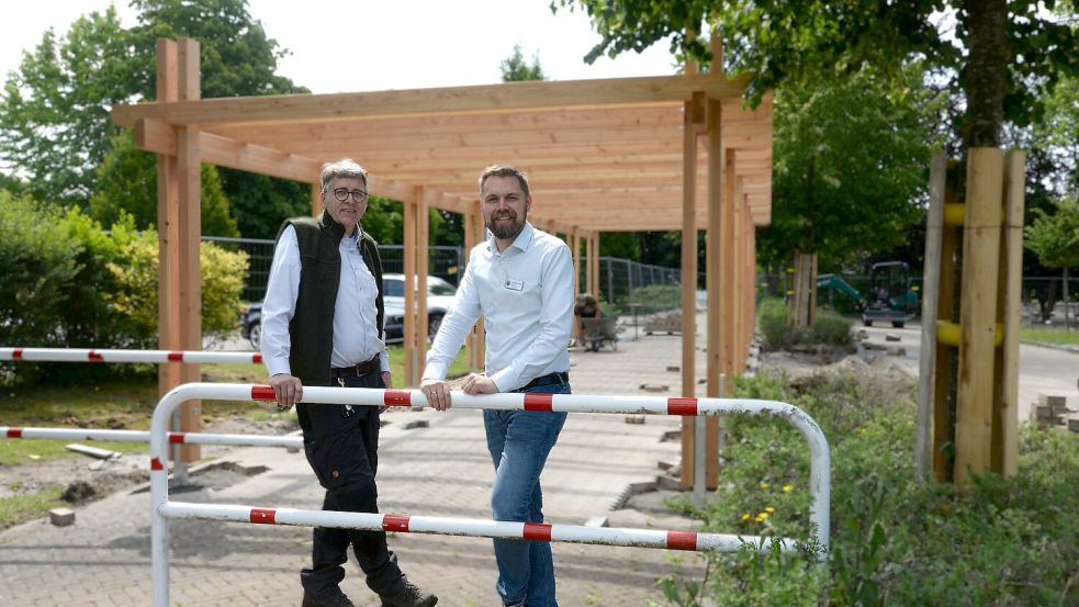 Eine große Holzkonstruktion überspannt den Ostfriesland-Wanderweg, der über den Platz verläuft. Sie soll dazu einladen, auf dem Platz eine Rast einzulegen. Schon vor dem Platz sollen Zeitzeichen („noch 1000 Jahre“) auf die Ausstellung aufmerksam machen. Bürgermeister Gerd Dählmann (links) und Gemeindedirektor Joachim Duin sind begeistert, dass die Arbeiten gut vorangehen. Foto: Karin Lüppen