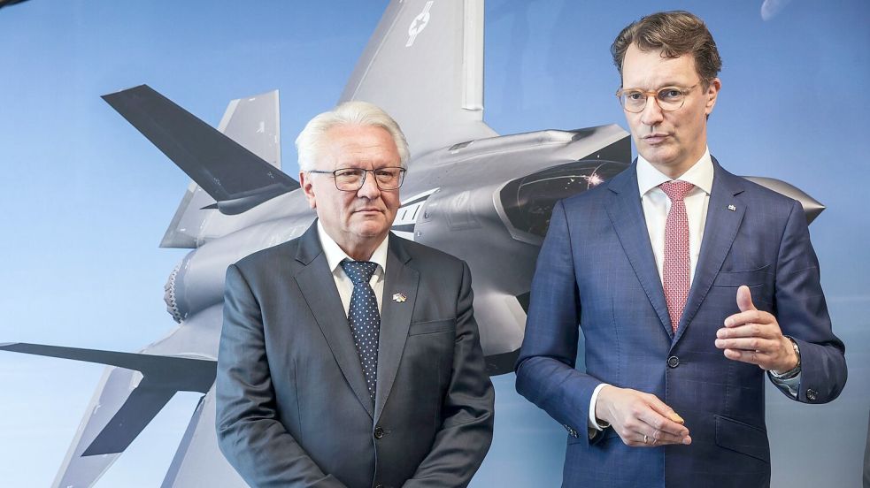 Papperger und Wüst vor einem Bild des F-35-Flugzeugs. Ende nächsten Jahres soll das erste Rumpfmittelteil dieses Tarnkappenbombers in Weeze fertig sein. Foto: Oliver Berg/dpa