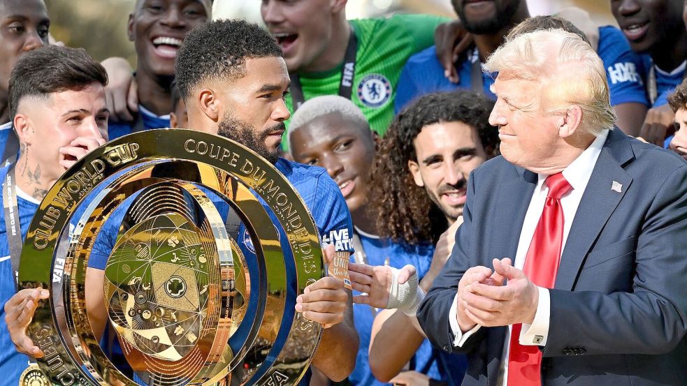 Chelseas Kapitän Reece James (l/vorn) hält auf dem Siegerpodest die Trophäe in den Händen und schaut irritiert zu US-Präsident Donald Trump. Foto: Sven Hoppe/dpa