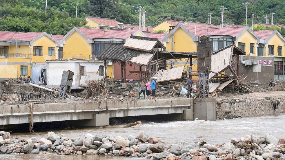 Dorfbewohner versammeln sich in der Nähe einer Brücke, die nach schweren Regenfällen im Bezirk Miyun am Stadtrand von Peking überflutet wurde. Foto: Andy Wong/AP/dpa