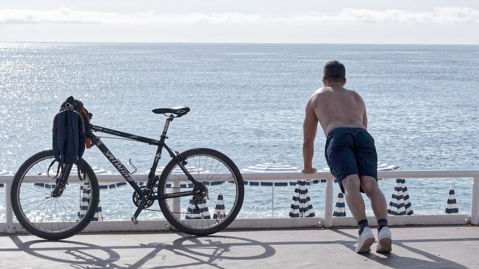 Ein Mann mit nacktem Oberkörper macht am Strand von Nizza neben seinem Fahrrad Übungen. (Archivbild) Foto: Serge Haouzi/XinHua/dpa