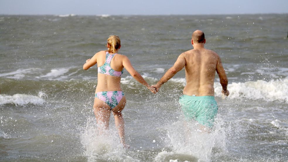 Teilnehmer rennen beim Neujahrsbaden Hand in Hand ins Wasser. Foto: Volker Bartels/dpa