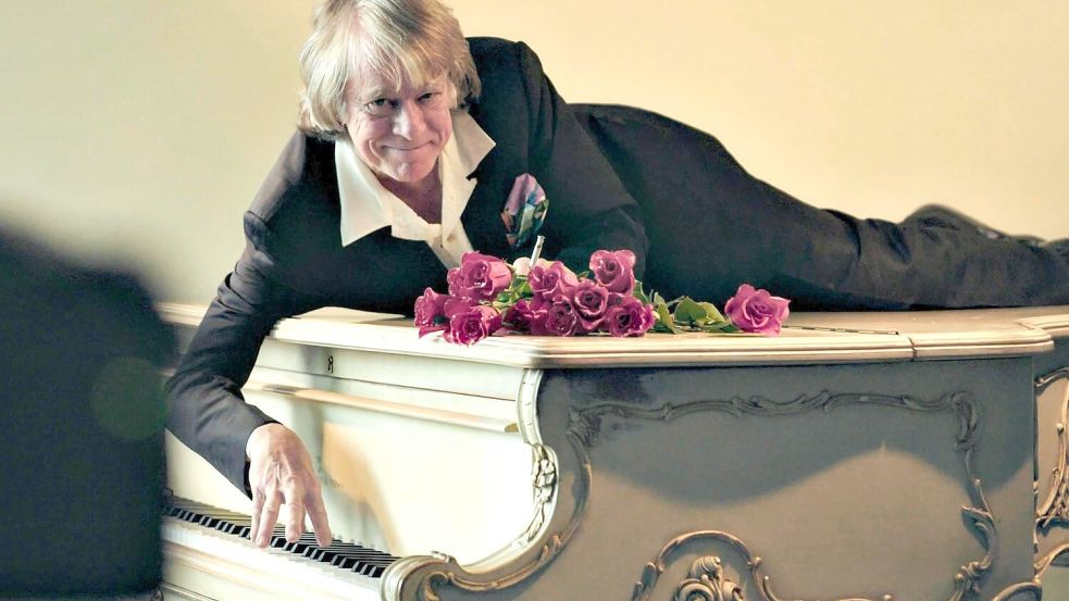 Helge Schneider liegt auf einem Klavier in einer Szene des Films „Helge Schneider - The Klimperclown“, der nun in der Mediathek zu sehen ist und am Mittwoch, 20.8., im Ersten gezeigt wird. Foto: -/SWR Presse/Bildkommunikation/dpa