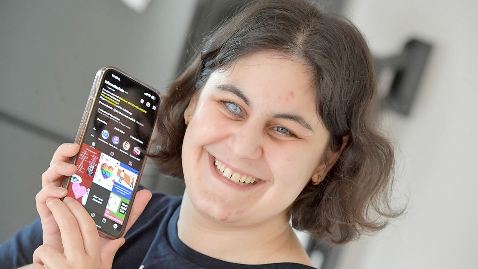 Barrierefrei posten in den sozialen Medien ist nicht schwer, sagt Mira Frei aus Hage. Trotzdem machen es die wenigsten – nicht mal bei Nachrichten. Auf dem Bild ist Mira Frei zu sehen, wie sie lächelnd ihr Smartphone neben ihr Gesicht hält. Mira Frei ist eine junge Frau mit kinnlangen dunklen Haaren. Auf dem Display ist ihr Instagram-Account erkennbar. Foto: Klaus Ortgies
