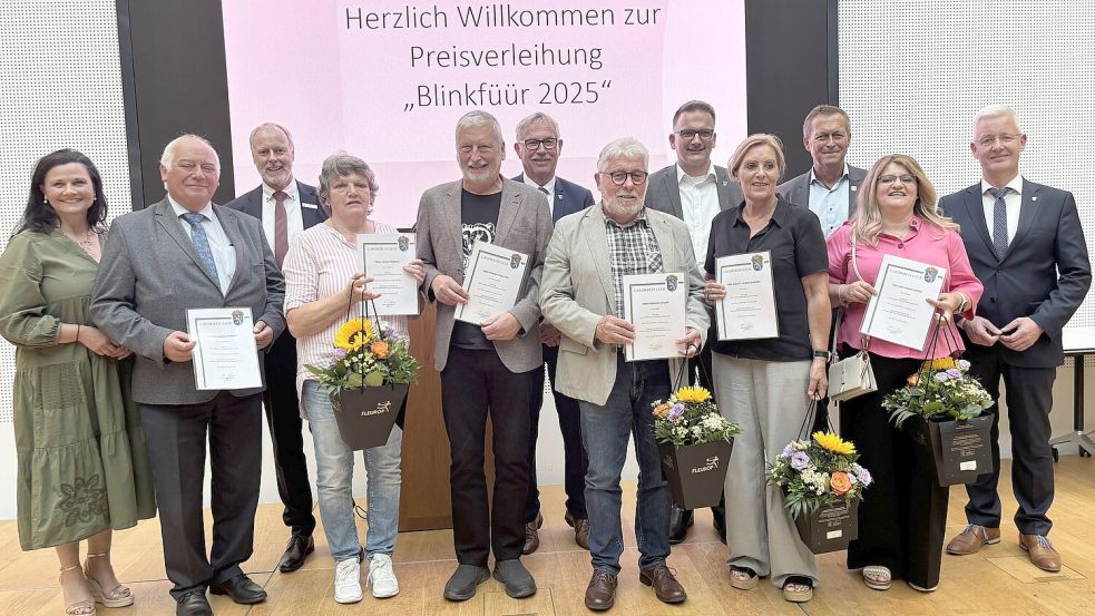 Die Ausgezeichneten des Blinkfüür 2025 mit den Laudatoren Matthias Groote (rechts) und Gitta Connemann (links), Bürgermeistern oder Stellvertretern sowie Sparkassen-Vorstand: Bernhard Robbers (vordere Reihe, ab Zweitem von links), Helga Frerichs, Werner Lambertus Stalljann, Gerhard Willms, Brigitt Hejnal-Modder und Ana-Maria Andrei. Es fehlt Jürgen Müller. Foto: Jonas Bothe