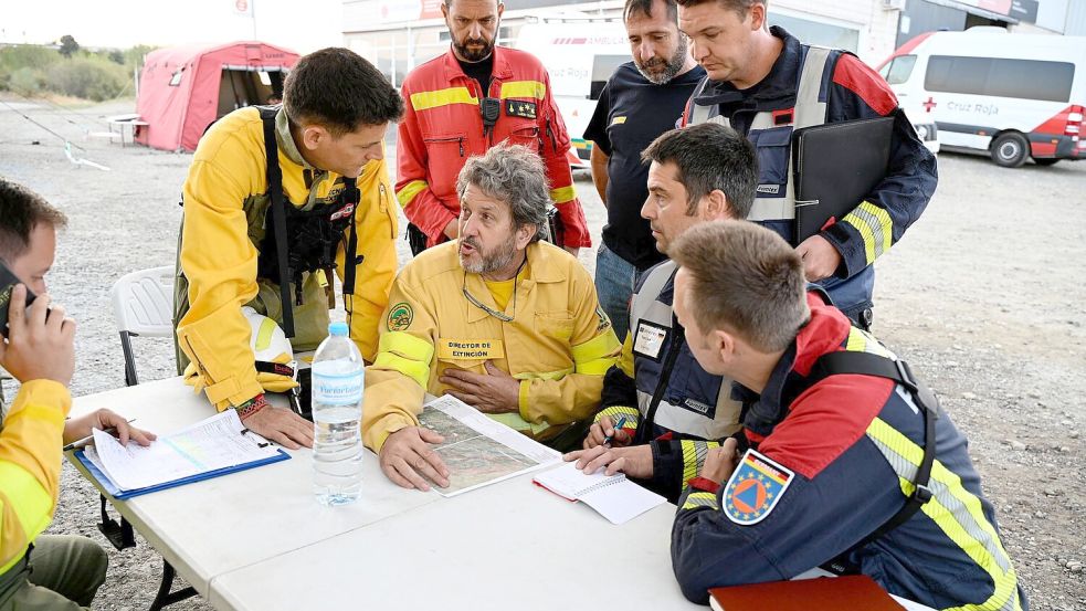 Spanische und aus Deutschland zur Hilfe geeilte Feuerwehrleute beraten bei dem Ort Jarilla über die Bekämpfung eines großen Waldbrandes. (Archivbild) Foto: Sven Käuler/dpa