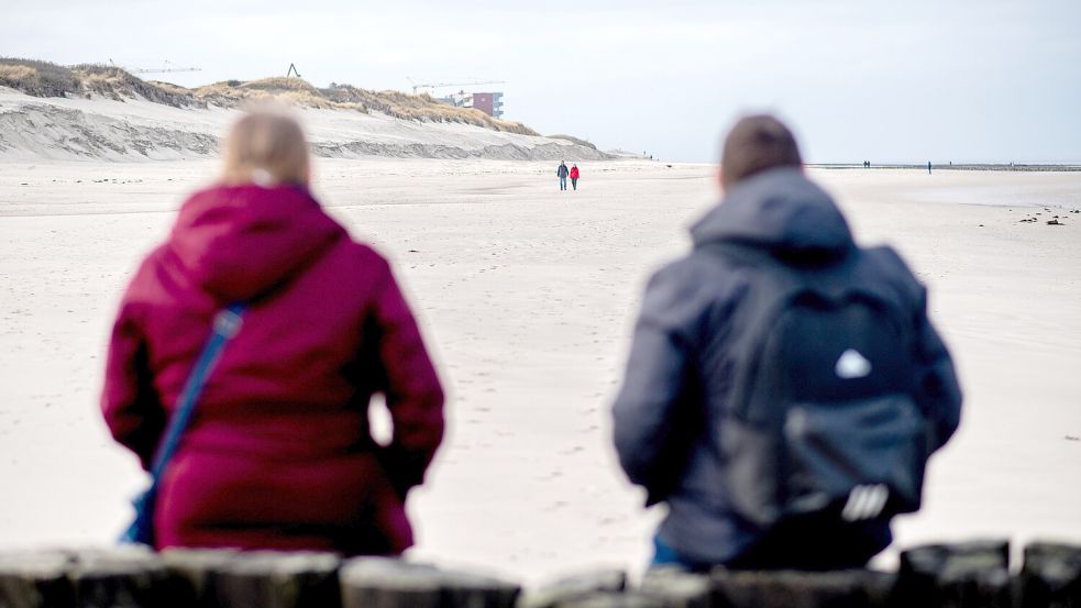 Ein Mann und eine Frau sitzen auf den Holzpfählen einer Buhne am Strand der Insel Wangerooge. Foto: Hauke-Christian Dittrich/dpa