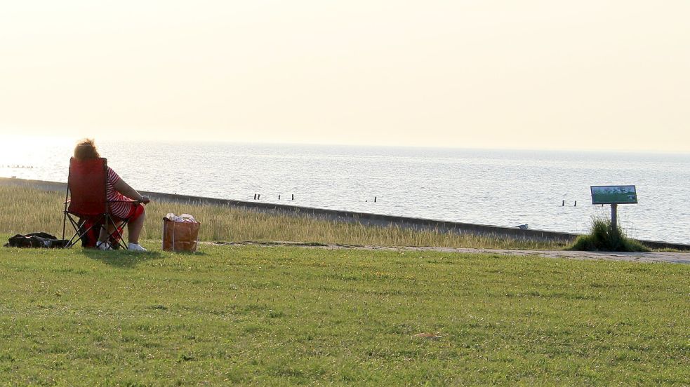 Eine Frau sitzt in Harlesiel am Wasser und genießt das Wetter. Foto: Imke Oltmanns