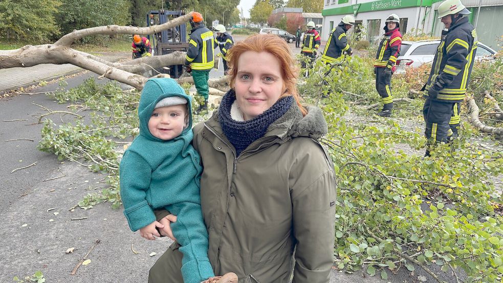 Die Ihrhoverin Rebecca Baktash und ihr eineinhalb Jahre alter Sohn Elias stehen vor dem Baum, der mittlerweile von Einsatzkräften der Feuerwehr Ihrhove beseitigt wird. Der Baum war einige Minuten zuvor von einer Windböe erfasst worden und dann auf die Straße gefallen. Genau in dem Moment waren Mutter und Sohn noch im Wagen unterwegs, die Ihrhoverin konnte rechtzeitig bremsen und kam kurz vor dem Baumstamm zum Stehen. Foto: Carsten Ammermann