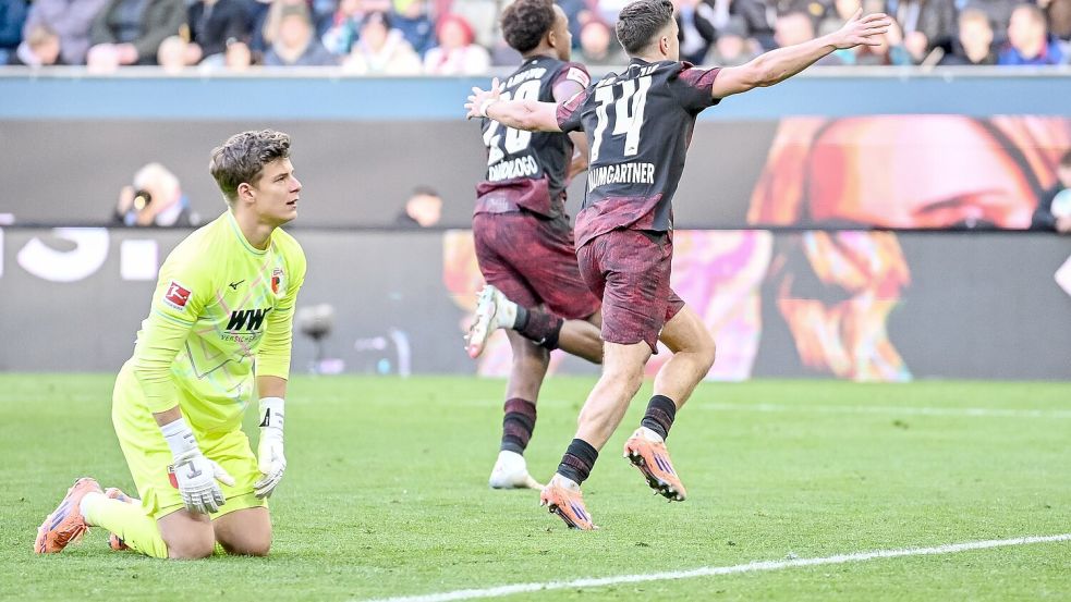 Augsburgs Torwart Finn Dahmen kauert bedröppelt am Boden, die Leipziger Assan Quedraogo (M) und Christoph Baumgartner (r) bejubeln das 0:5. Foto: Harry Langer