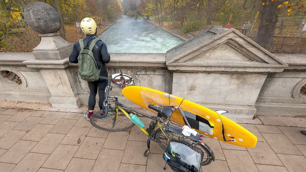 Ein Mann mit einem Surfboard an seinem Fahrrad schaut von einer Brücke auf die - nicht mehr vorhandene - Eisbachwelle im Englischen Garten. Foto: Peter Kneffel/dpa