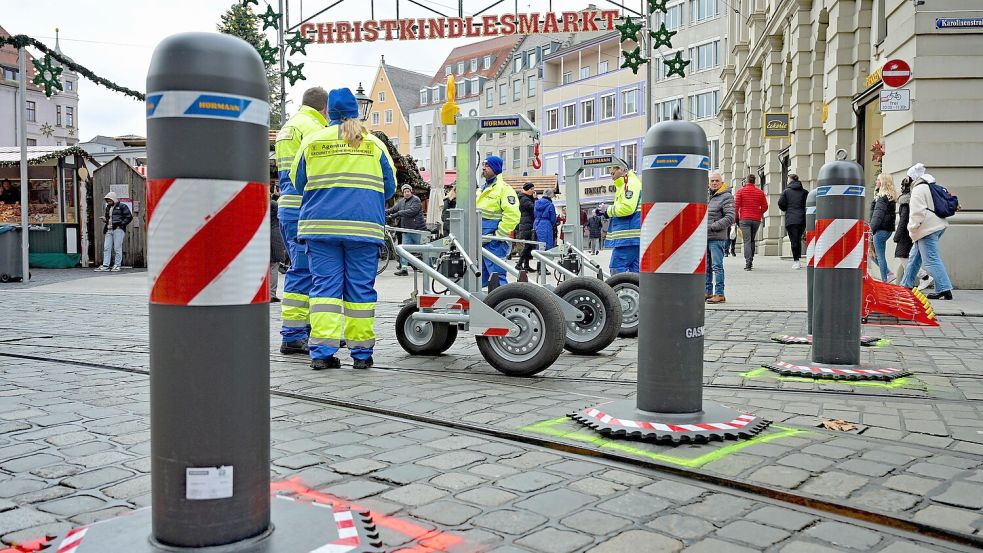Arbeiter verschieben mobile Poller auf dem Christkindlesmarkt in Augsburg, damit die Straßenbahn durchfahren kann. Foto: dpa/Malin Wunderlich