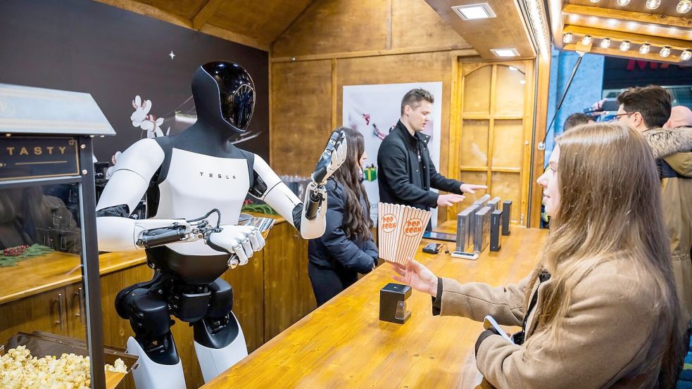 Der humanoide Roboter „Optimus“ von Tesla verteilt bei seiner Vorstellung in der Mall of Berlin Popcorn an eine Besucherin. Foto: Christoph Soeder/dpa