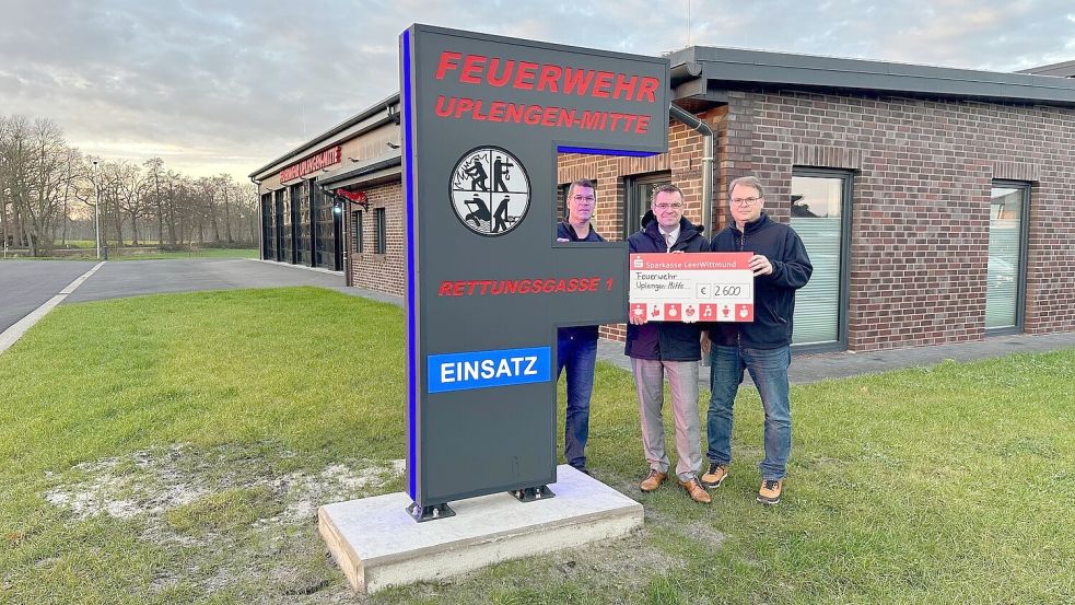 Die Pylone ist nicht zu übersehen – umso mehr, wenn es in den Einsatz geht. Ortsbrandmeister Uwe Glania (von links), Ingo Fortkamp von der Sparkasse sowie der stellvertretende Ortsbrandmeister Stephan Tuitjer präsentieren den Scheck, der die Fördersumme zeigt. Foto: privat