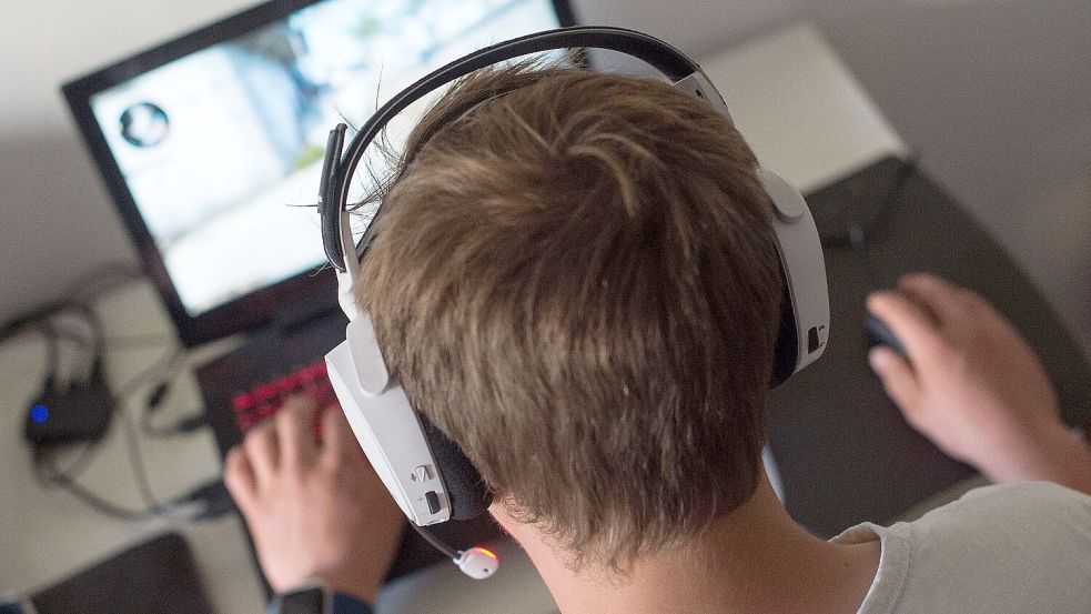 Ein junger Mann sitzt mit einem Headset vor einem Laptop und spielt ein Online-Computerspiel. Foto: DPA