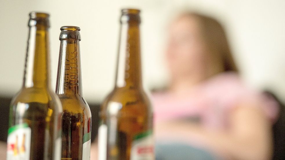 Ein Mädchen sitzt hinter leeren Bierflaschen. Foto: Alexander Heinl/DPA