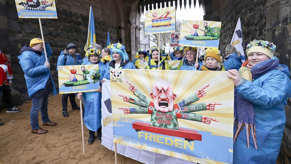 Der ukrainische Hilfsverein Blau-Gelbes-Kreuz hält Plakate mit Putin-Motiven hoch. Das ist als Zeichen der Solidarität mit Wagenbauer Jacques Tilly gemeint. Dieser wird in Russland strafrechtlich verfolgt. Foto: Oliver Berg