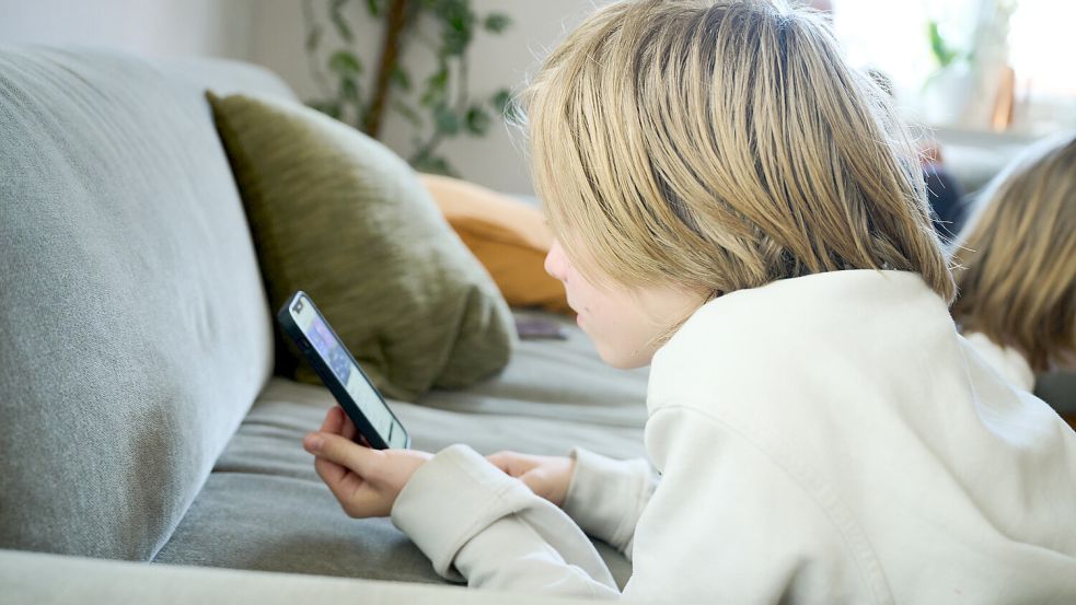 Ein Junge liegt auf einem Sofa und guckt auf sein Smartphone. Foto: DPA