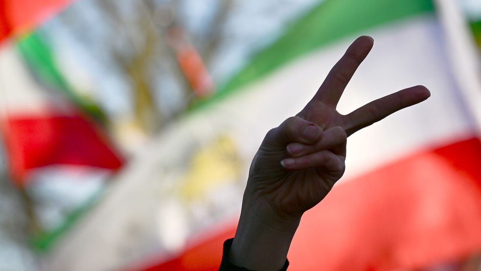 Berlin: Eine Teilnehmerin einer Demonstration gegen das iranische Mullah-Regime zeigt nahe der Botschaft Israels vor iranischen Fahnen das Victory-Symbol mit ihrer Hand. Foto: Sebastian Christoph Gollnow/dpa