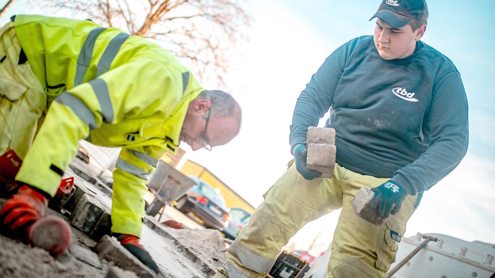 Gutes Miteinander: Tiefbauhelfer Rustam Morokhovych (rechts) reicht seinem Kollegen Raphael Duscha Steine an. Sie pflastern nach Arbeiten im Versorgungsnetz. Foto: Ole Cordsen/TBD