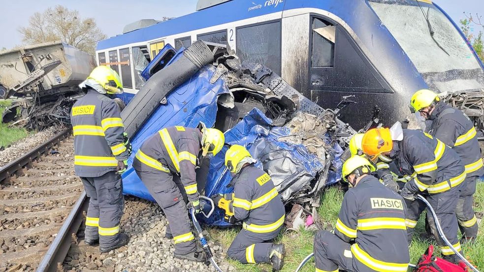 Feuerwehrleute arbeiten am Unglücksort, wo ein Personenzug und ein Lastwagen zusammengestoßen sind. Bei dem Unglück kam eine Person ums Leben, 21 Menschen wurden verletzt. Foto: -