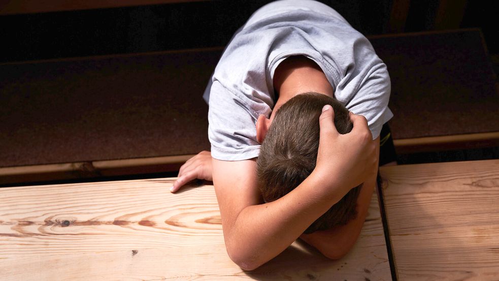 Ein Kind versteckt sein Gesicht unter seinen Armen und liegt mit dem Kopf auf einem Tisch (gestellte Szene). Foto: dpa