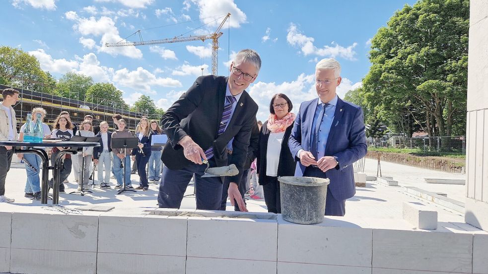 Bürgermeister Heiko Abbas (von links), Anja Meißner, Leiterin der Grundschule Weener, und Landrat Matthias Groote legten den Grundstein. Die Schüler der Bläserklasse und des Schulorchesters untermalten die Feier musikalisch. Foto: Tatjana Gettkowski