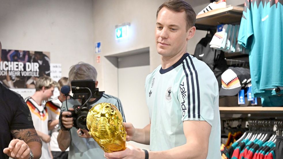 Lächelnd signiert Manuel Neuer einen goldenen WM-Pokal. Foto: Federico Gambarini/dpa