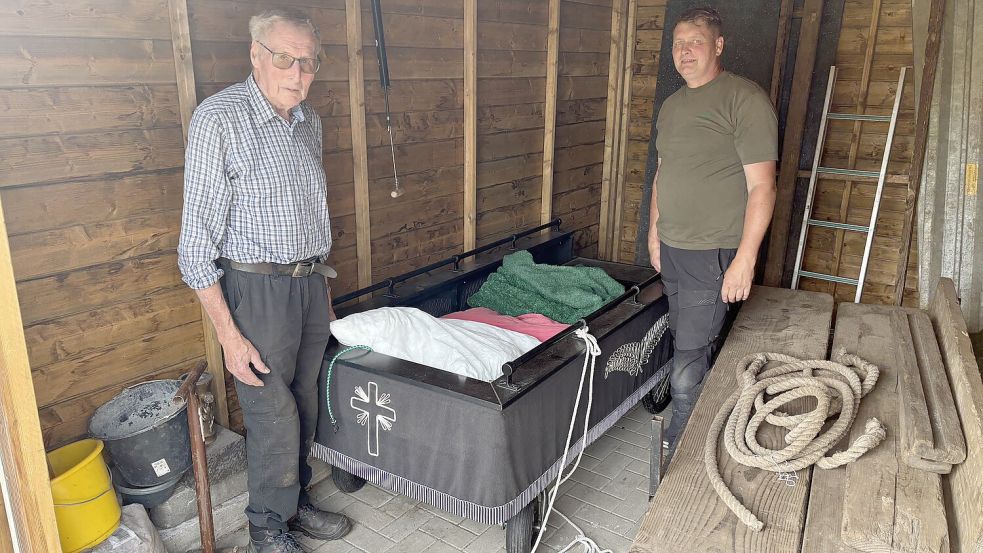 Johann Groenhagen (links) und sein Sohn Alfred Groenhagen, Inhaber der Ihrhover Firma Garten- und Landschaftsbau, stehen bei dem Grabwagen im Schuppen. Den Wagen hat ein Unbekannter wohl zweckentfremdet und darauf geschlafen. Der Einbrecher hatte sogar zwei Kopfkissen mitgebracht. Foto: Carsten Ammermann