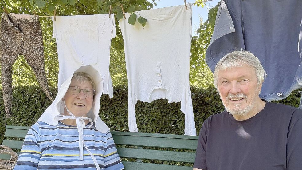 Gisela Wilken und Otto Klatt kennen sich mit der Kleidung früherer Generationen gut aus. Wilken hat eine Erntehaube aufgesetzt, im Hintergrund wehen ein Kittel, zwei Unterhemden und eine wollene Unterhose an der Leine – die typische Sommerkleidung der damaligen Zeit. Foto: Karin Böhmer