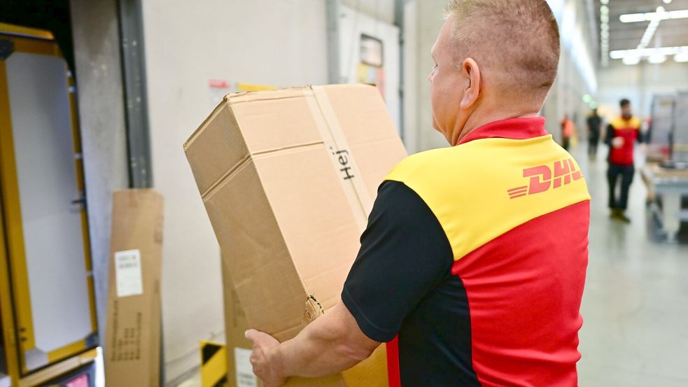 Ein Paketbote schleppt in einem DHL-Standort ein schweres Paket. (Archivbild) Foto: Sebastian Christoph Gollnow/dpa